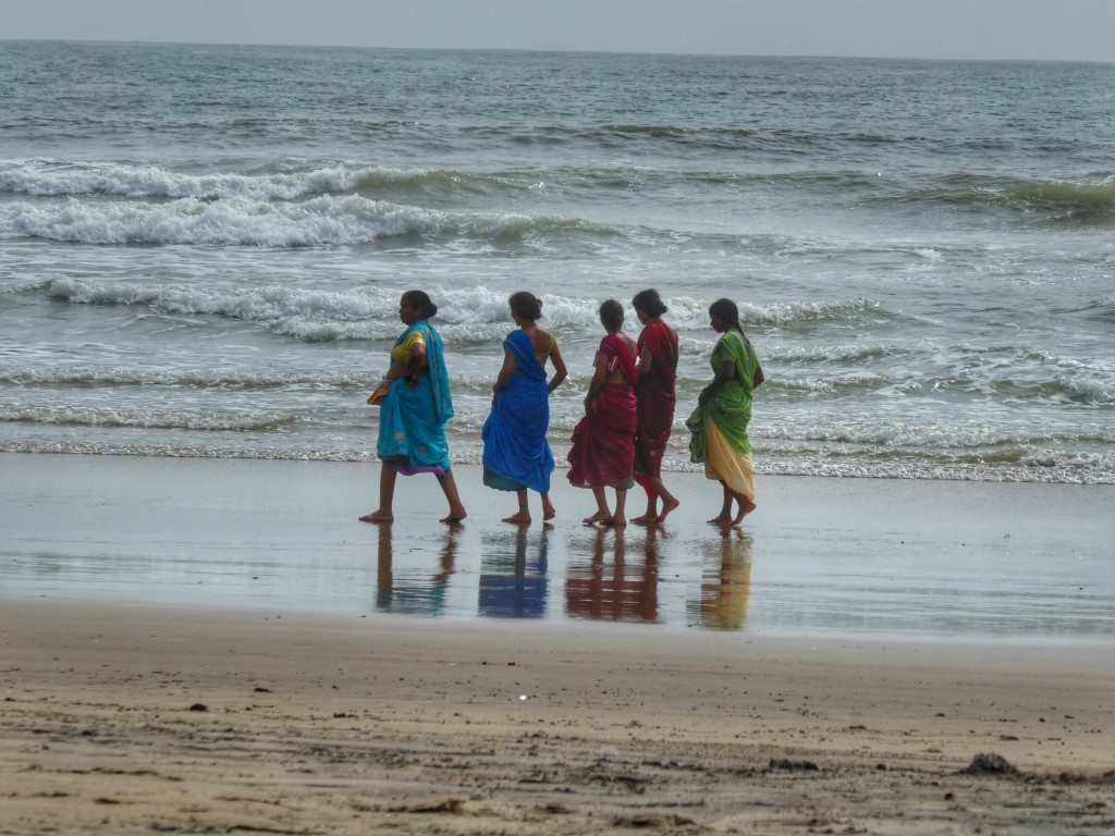 Indian ladies take a stroll on an almost desert Arambol beach in monsoon season